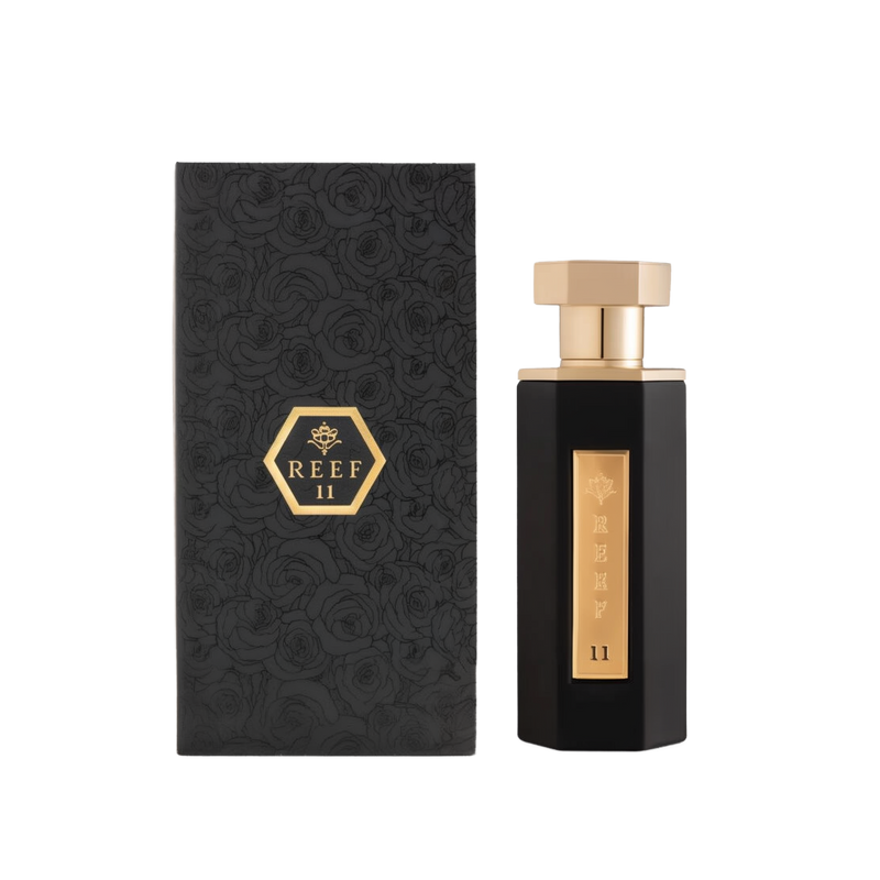 A sophisticated bottle of Reef 11 perfume by Reef Perfumes, displayed alongside its matching box. The bottle is tall and angular with a glossy black finish, featuring a vertical gold label engraved with 'REEF 11' and a crown emblem. It is topped with a geometric gold cap. The accompanying box is textured with an embossed rose pattern and features a gold hexagonal emblem with the fragrance name centered on the front, reinforcing the elegant and premium design