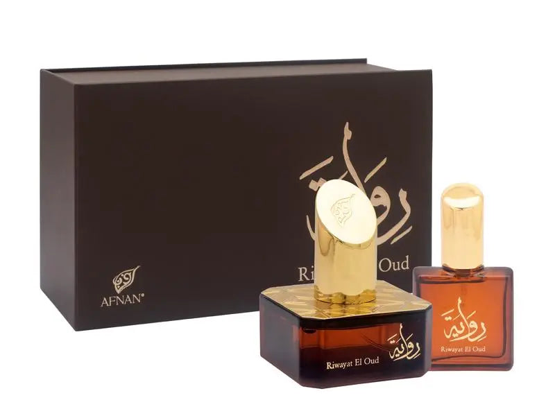 The image shows two perfume bottles with a rich, dark amber hue, set against a dark brown box that has the "AFNAN" logo in gold in the lower left corner. The box features a golden calligraphic design, likely Arabic script, which is presumed to be the name of the fragrance. The larger bottle has a square base with a distinctive, intricate gold pattern around the neck, and a circular gold cap embossed with a floral design.