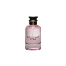 The image shows a bottle of "Rose of Dreams" eau de parfum by Zimaya. The perfume bottle is cylindrical with a soft pink hue and a clear glass bottom. It features a black cap with a gold band. The front of the bottle has black text that reads "ROSE OF DREAMS" and "zimaya." The overall design is elegant and minimalist, with the soft pink color evoking a sense of femininity and romance.