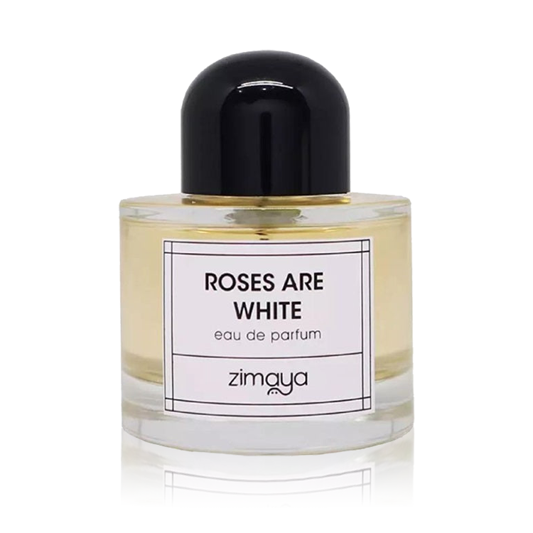 The image shows a bottle of "Roses Are White" eau de parfum by Zimaya. The perfume bottle is cylindrical and made of clear glass, showcasing a pale yellow liquid inside. It features a simple, modern design with a black cap. The front of the bottle has a white label with black text that reads "ROSES ARE WHITE" and "eau de parfum," along with the brand name "zimaya" at the bottom.