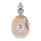The image shows a decorative perfume bottle:  The bottle has an ornate, multi-faceted glass design with a textured surface and a pale pink tint, suggesting a delicate fragrance within. It features a clear glass stopper with an intricate cut pattern on top. A metallic silver chain with a charm and a small black stone is attached to the neck of the bottle. The front of the bottle displays a white oval label with Arabic calligraphy and the name "ROUAT AL MUSK" in Roman characters below.