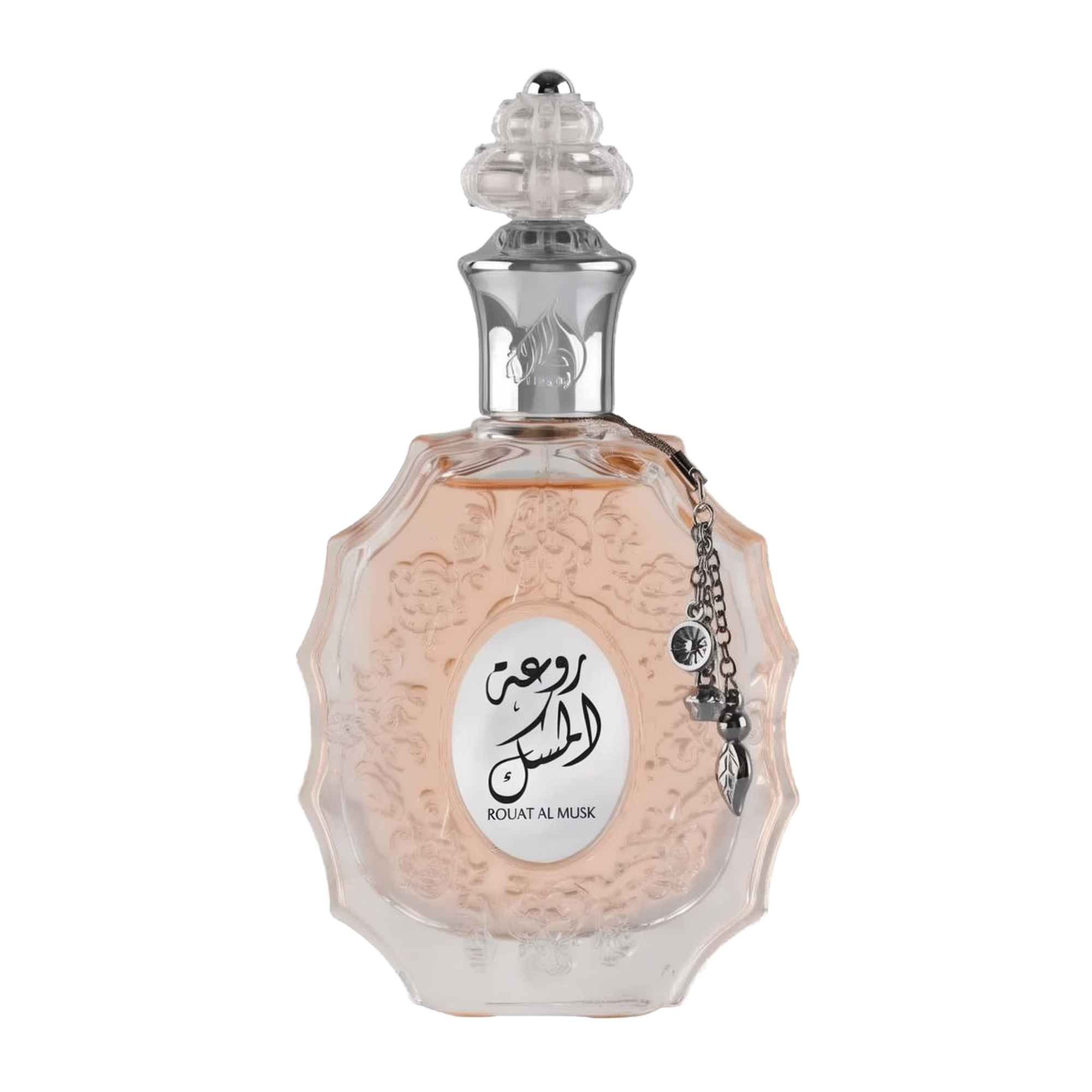 The image shows a decorative perfume bottle:  The bottle has an ornate, multi-faceted glass design with a textured surface and a pale pink tint, suggesting a delicate fragrance within. It features a clear glass stopper with an intricate cut pattern on top. A metallic silver chain with a charm and a small black stone is attached to the neck of the bottle. The front of the bottle displays a white oval label with Arabic calligraphy and the name "ROUAT AL MUSK" in Roman characters below.