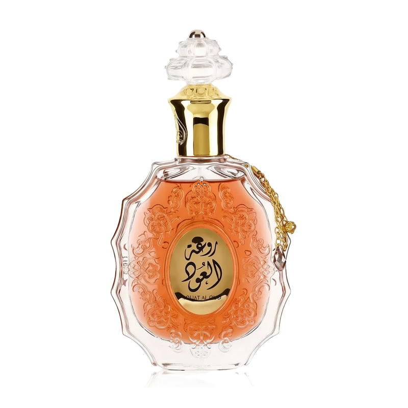 he image features an ornate perfume bottle:  The bottle is made of clear glass with a decorative texture and a central amber-colored panel. A clear and intricate glass stopper tops the bottle. A golden metallic chain with a charm is attached to the neck of the bottle. Arabic calligraphy is featured within the amber panel, and the name "ROUAT AL OUD" is inscribed in English below the calligraphy.