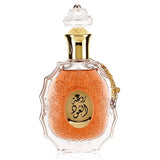 he image features an ornate perfume bottle:  The bottle is made of clear glass with a decorative texture and a central amber-colored panel. A clear and intricate glass stopper tops the bottle. A golden metallic chain with a charm is attached to the neck of the bottle. Arabic calligraphy is featured within the amber panel, and the name "ROUAT AL OUD" is inscribed in English below the calligraphy.