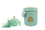 A round, Art Deco-style candle container in a tiffany blue color with a textured diamond pattern, topped with a gold-colored knob and adorned with a matching tiffany blue tassel. The container is accompanied by a cylindrical tiffany blue gift box with gold accents and a label that reads 'Côte Noire' in an elegant script. The box also features a gold emblem and a hanging tag.