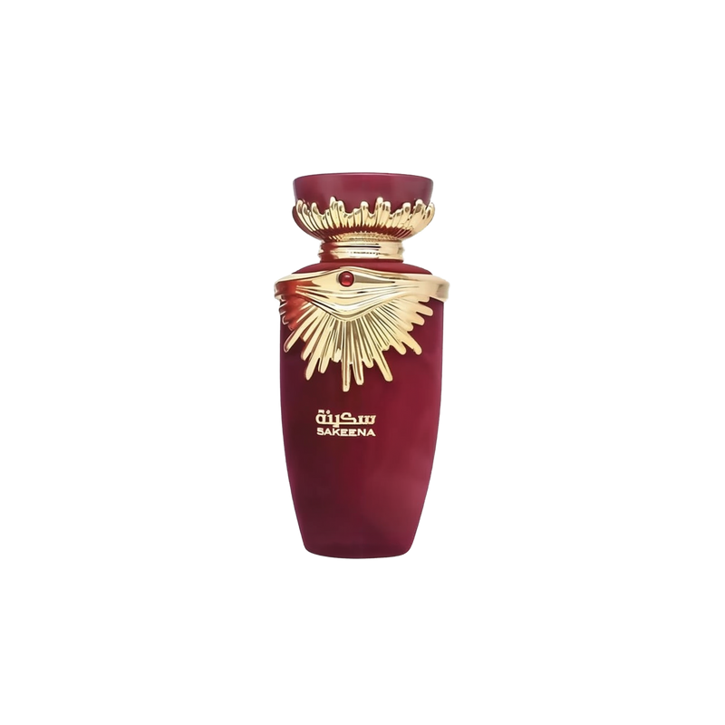 The image shows a perfume bottle from the brand Lattafa, specifically the "SAKEENA" fragrance. The bottle is maroon with a tapered shape and features a golden, ornate lid that resembles a crown, complete with a gemstone accent in the center. The design elements suggest a luxurious and exotic scent. "SAKEENA" is written in gold Arabic calligraphy on the body of the bottle, which is set against a plain background, emphasizing the bottle's elegant design and rich color palette.