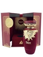 The image features an elaborate perfume presentation of "SAKEENA" by Lattafa. The box is a deep burgundy color with golden accents and a geometric, radial design emanating from a circular emblem that reads "SAKEENA" in Arabic script. Inside the box, the perfume bottle is revealed—a luxurious maroon vessel with a golden, crown-like lid embellished with a gemstone. The bottle rests on a velvet-like fabric, enhancing the feeling of opulence. On the front of the bottle, "SAKEENA" is written in Arabic.