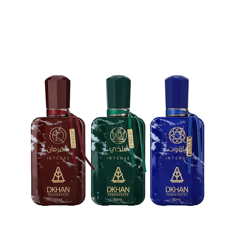 This image features a set of three distinct perfume bottles from DKHAN Fragrances, each containing 50ml of Eau de Parfum. From left to right: the first bottle is maroon with a matching geometric cap and a gold tag, the second bottle is emerald green with a gold tag, and the third is cobalt blue with a gold tag. Each bottle has a marbled effect and is adorned with the DKHAN logo and 'INTENSE' in gold lettering, along with the brand's emblem, a heart within a diamond shape.