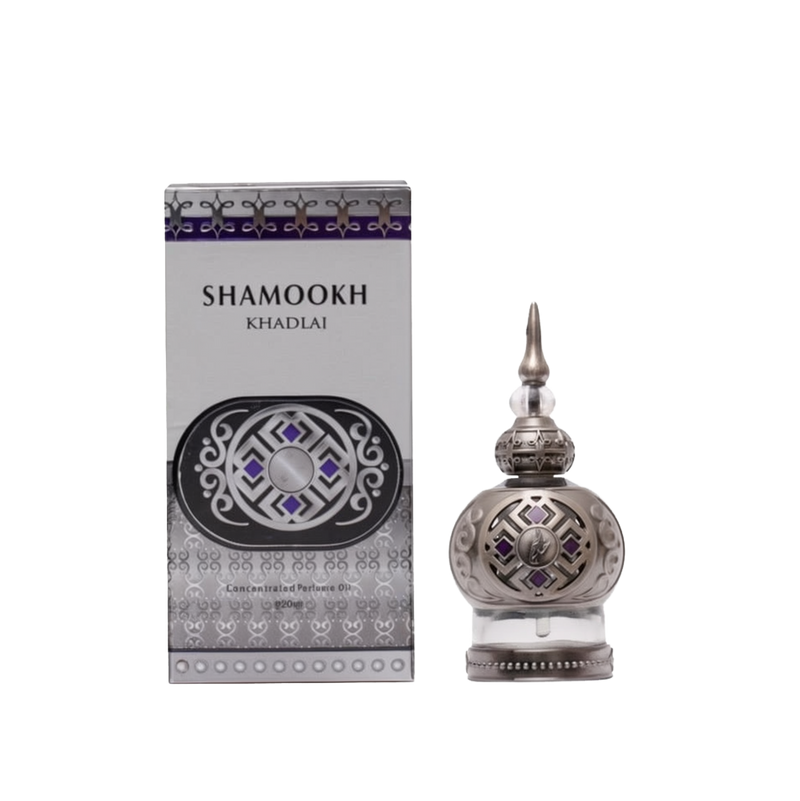 The image shows a product called "Shamookh" by Khadlaj, which is a concentrated perfume oil. The perfume comes in a 20ml spherical bottle with a silver finish, featuring intricate patterns and a pointed cap that adds a touch of elegance. The design includes decorative elements with purple accents, enhancing its luxurious appearance. The packaging box matches the bottle's design, with a silver and purple theme, featuring the product name "Shamookh" in bold letters and additional ornamental details.