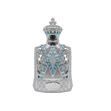 The image depicts a highly ornate perfume bottle with a design that mimics the aesthetic of royal regalia. The bottle is predominantly silver with intricate filigree work and is adorned with a pattern of bright blue gemstones arranged in V-shaped lines along the front. The neck and shoulder of the bottle are also embellished with blue gems and delicate silver patterns, leading up to a crowned cap that features similar gemstones and a studded pattern.