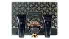 The image features a luxurious bath and body set from the "SOUVENIR Desert Rose" collection by Afnan. The set includes a spherical golden perfume bottle with a clear dome top, flanked by two navy blue tubes—one labeled as "ENERGIZING SHOWER GEL" and the other as "LUSTEROUS NATURAL BODY LOTION". Each product has gold lettering and rose accents. The background and base of the set feature an elegant pattern of gold roses on a dark, forest green backdrop.