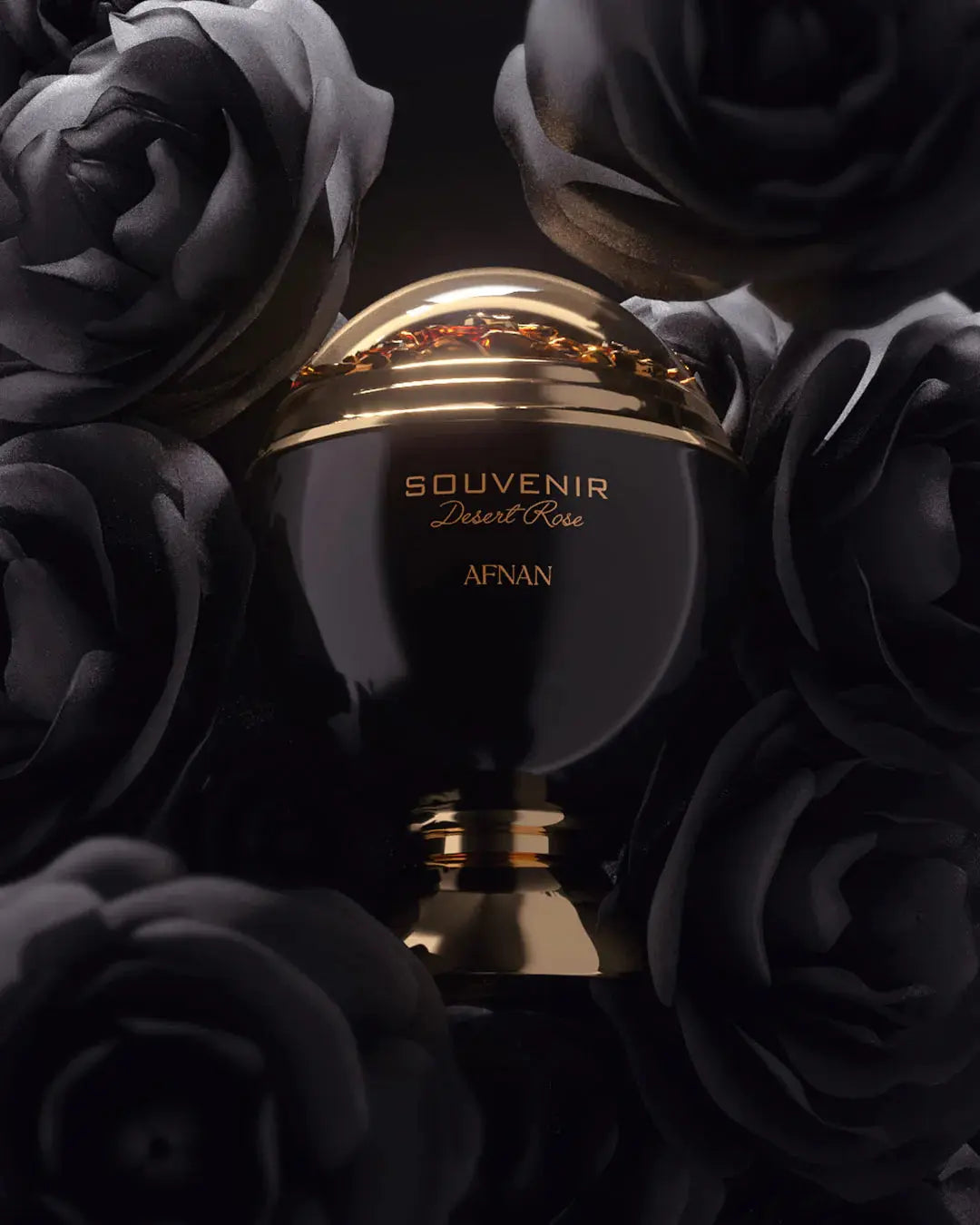 The image features a luxurious perfume bottle, named "SOUVENIR Desert Rose AFNAN", nestled amongst dark, moody roses. The bottle has a spherical, matte black body with a golden band around its midsection, and the top half is a clear dome revealing a shimmering substance within. The bottle's base is also gold, adding to its opulent appearance. The roses surrounding the bottle have a deep black hue, giving the composition a rich, dramatic contrast.