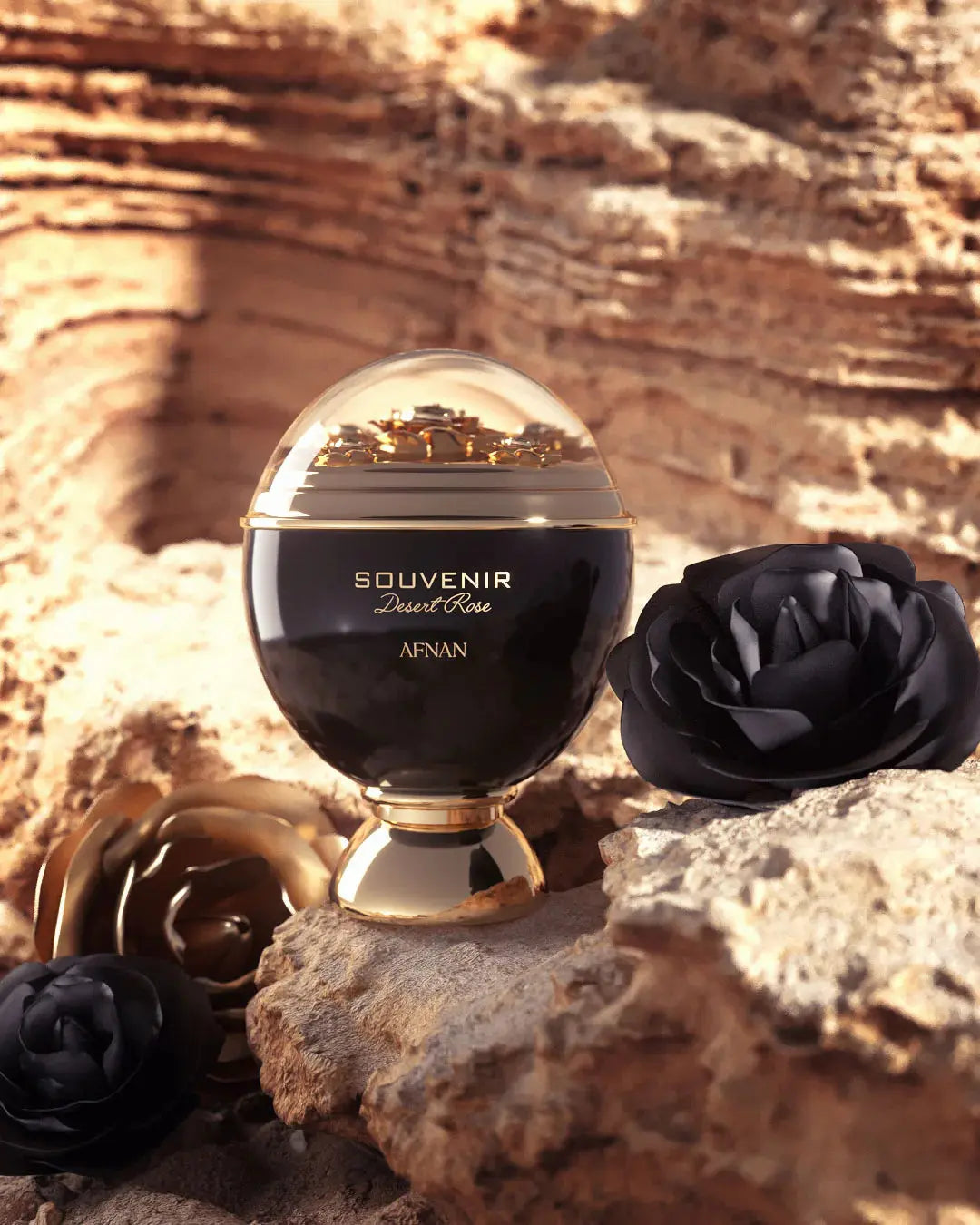 The image depicts an elegant perfume bottle placed on a rocky desert-like terrain, resonating with the name "SOUVENIR Desert Rose AFNAN" inscribed in gold on the bottle's black surface. The bottle has a rounded base and is topped with a clear dome that encases golden flakes, giving the impression of a miniature desert landscape.