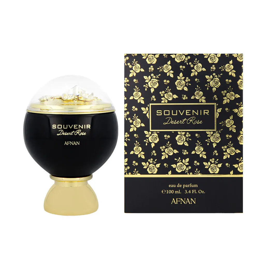 The image showcases a perfume set that includes a bottle and its packaging. The perfume bottle has a matte black spherical base with a clear dome on top, revealing what appears to be gold flakes or particles inside.  Beside the bottle is its box, featuring an elegant black background with a floral pattern of golden roses and leaves.