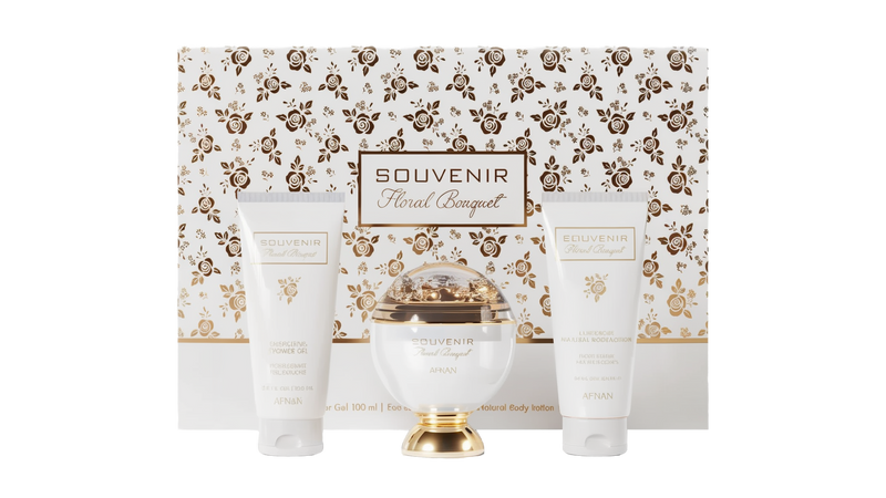 A gift set of the Souvenir Floral Bouquet by Afnan Perfumes. The packaging features an elegant floral design in gold and white. The set includes a luxurious perfume bottle with a gold and white design, an Energizing Shower Gel, and a Lusterous Natural Bod