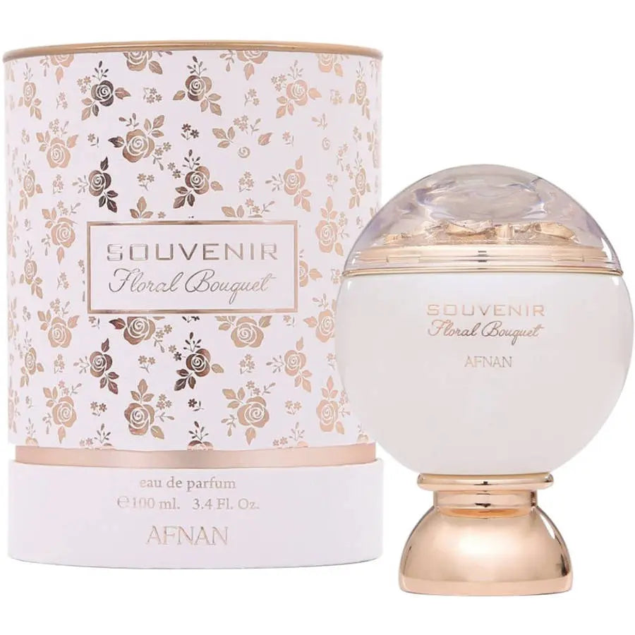 The image displays a perfume bottle and its cylindrical packaging. The bottle has a spherical white body with "SOUVENIR Floral Bouquet AFNAN" written in a gentle script. It features a clear dome on top, under which a golden substance can be seen, giving a luxurious touch to the design. The packaging repeats the rose gold theme with a soft pink and gold floral pattern.  The overall design of the product and packaging evokes a sense of delicate, luxury and femininity.
