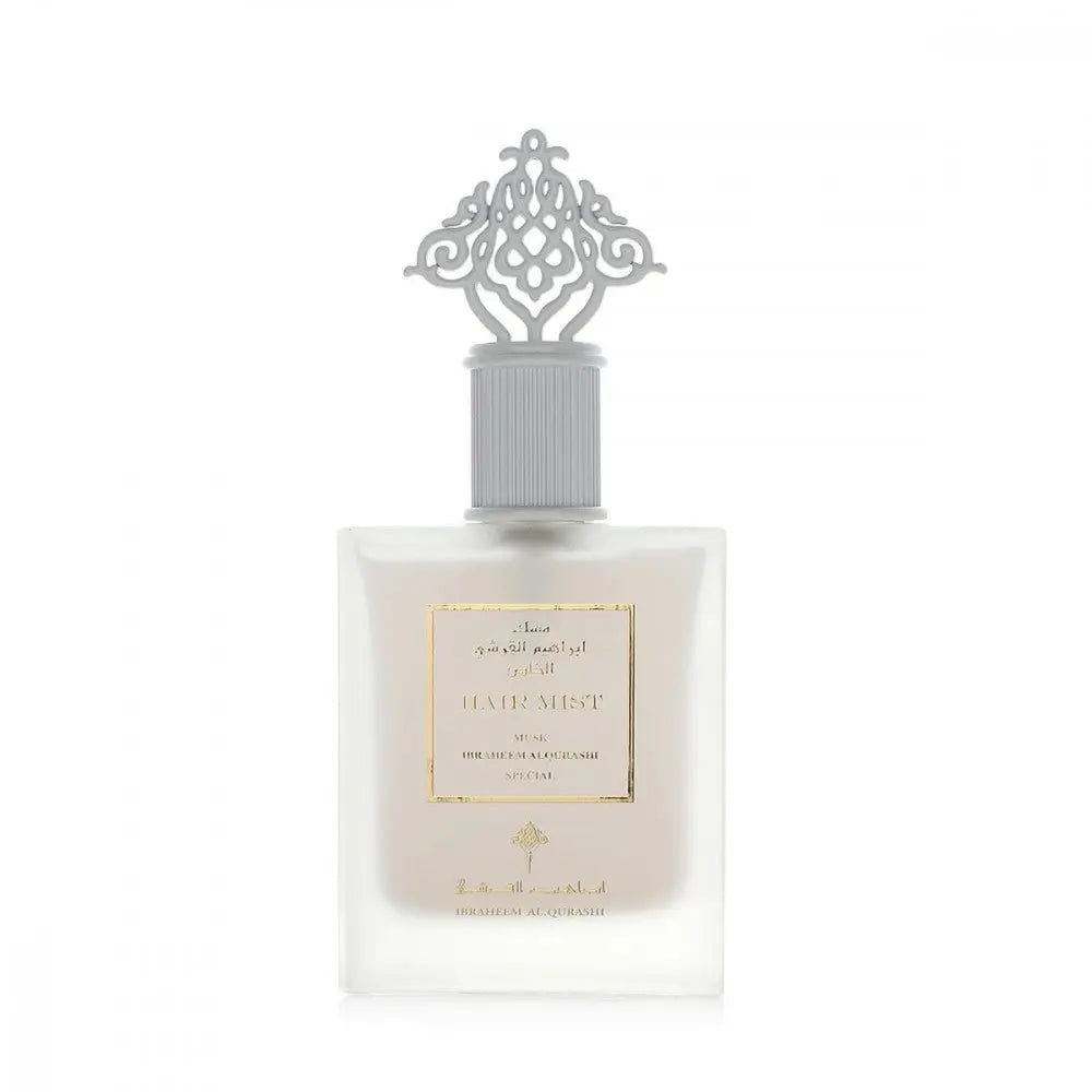 The image shows a square-shaped, frosted glass perfume bottle with a white ornate cap featuring a design reminiscent of Middle Eastern or Islamic art. The bottle has a gold-framed label with the words "HAIR MIST MUSK IBRAHEEM ALQURASHI SPECIAL" The label's elegant typography and the cap's intricate pattern contribute to the product's luxurious appearance. The overall design suggests that it is a special hair mist fragrance from the Ibraheem AlQurashi brand.