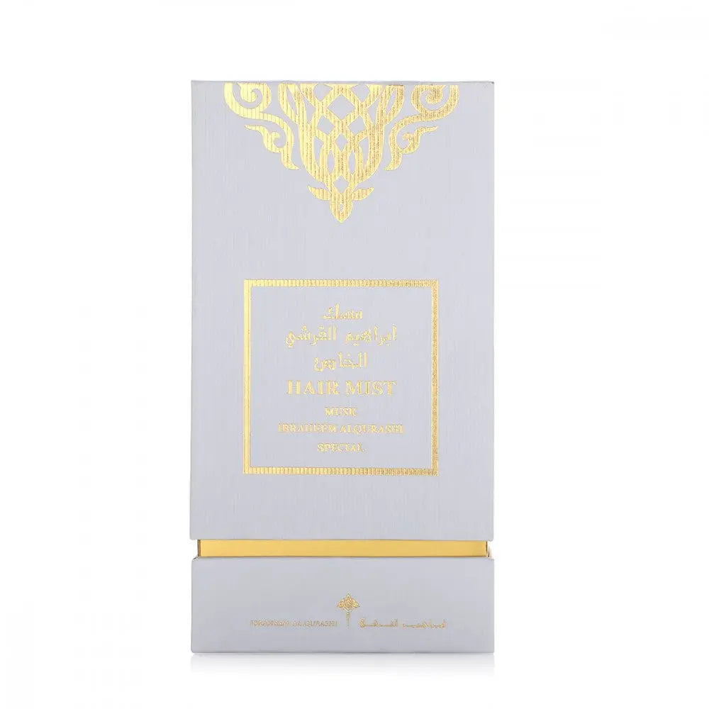 The image features a tall, grey packaging box for a hair mist product. The box is adorned with a golden ornamental design at the top and a gold-framed label in the center that includes both English and Arabic texts. The texts read "HAIR MIST MUSK IBRAHEEM ALQURASHI SPECIAL." A gold band accents the bottom of the box, and the brand's logo, "IBRAHEEM AL.QURASHI," is printed near the lower edge.