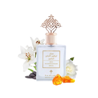 A bottle of 'Special Musk' by Ibraheem Al Qurashi, with a sophisticated design. The perfume bottle is square with a soft blue color and a rose gold ornate cap that features an intricate lattice design. The label has Arabic calligraphy and English text. It is presented with a backdrop of white flowers, possibly lilies, and a white rose, along with two amber-colored resin pieces in front, suggesting a luxurious and aromatic product.