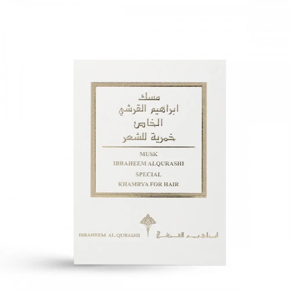The image shows a white packaging box for a fragrance product, with elegant gold and black text and decorative borders. The text includes both English and Arabic scripts that read "MUSK IBRAHEEM AL.QURASHI SPECIAL KHAMRIYA FOR HAIR." The packaging is clean and sophisticated, with a small logo at the bottom, suggesting that it contains a special musk fragrance designed for hair.