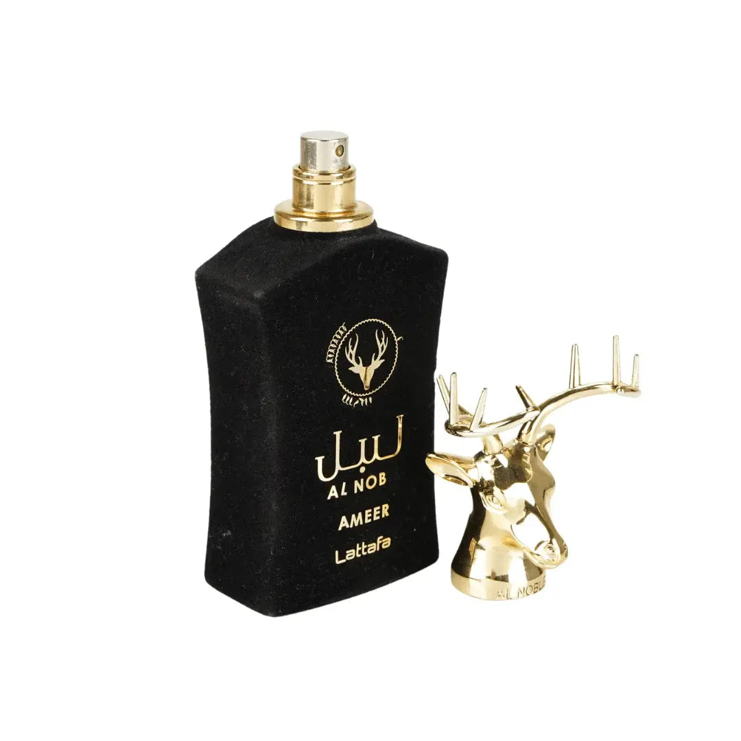  The image shows a perfume bottle named "AL NOB AMEER" by Lattafa. The bottle is black with a velvety texture and has gold lettering for the brand logo and name, giving it a luxurious appearance. Next to the bottle is a shiny, metallic gold cap in the shape of a deer's head with elaborate antlers, detached from the bottle. The cap's intricate design and golden sheen suggest a premium and exotic fragrance contained within. 