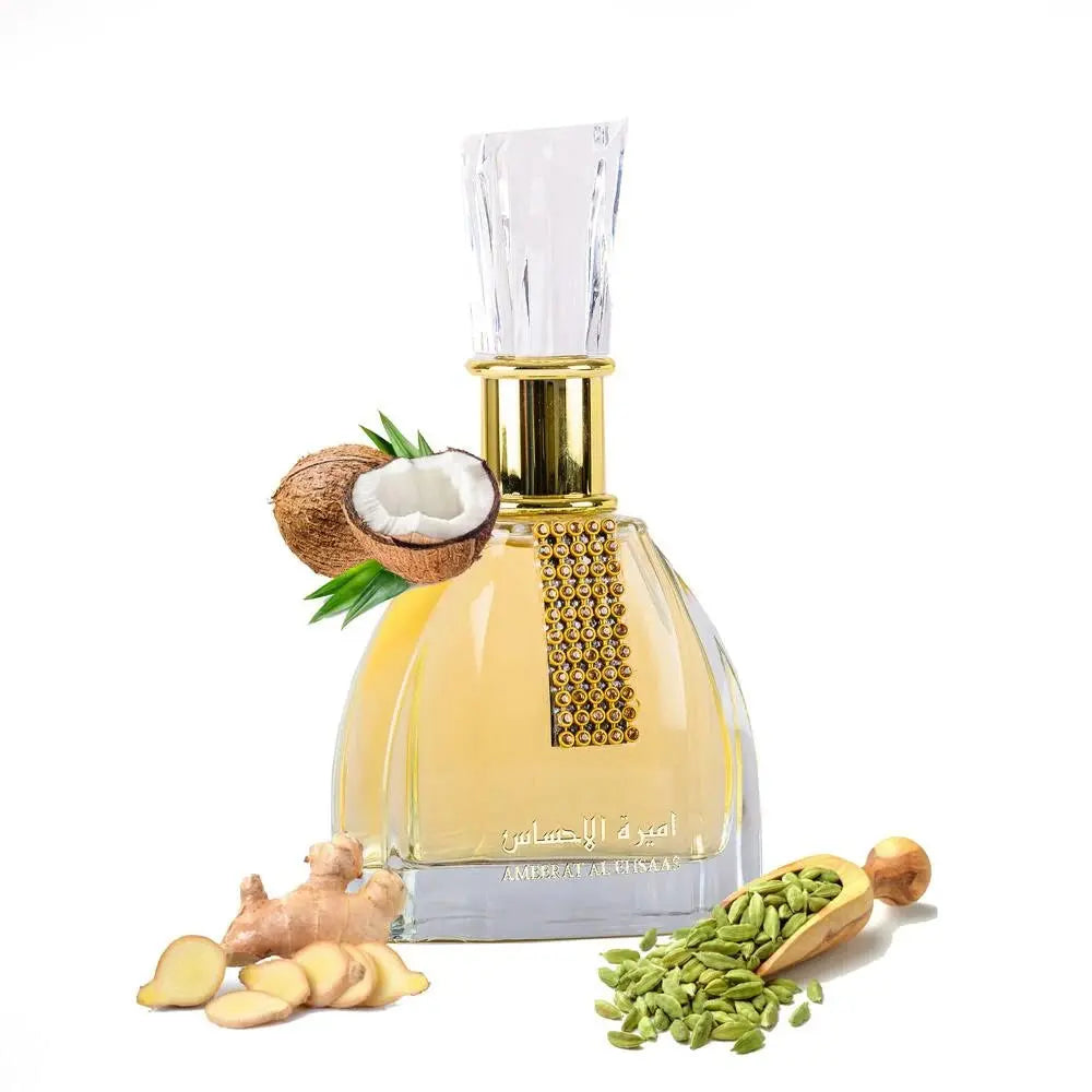 The image is of a perfume bottle titled 'Ameerat Al Ehsaas' from 'Ard Al Zaafaran'. The clear glass bottle has a wide base and narrows slightly towards the top, with a large, faceted clear glass cap. The perfume liquid appears to be a light yellow color. Around the bottle are ingredients that suggest the scent notes: a halved coconut with its white flesh visible, a piece of ginger root with slices in front of it, and a wooden scoop filled with green cardamom pods. 