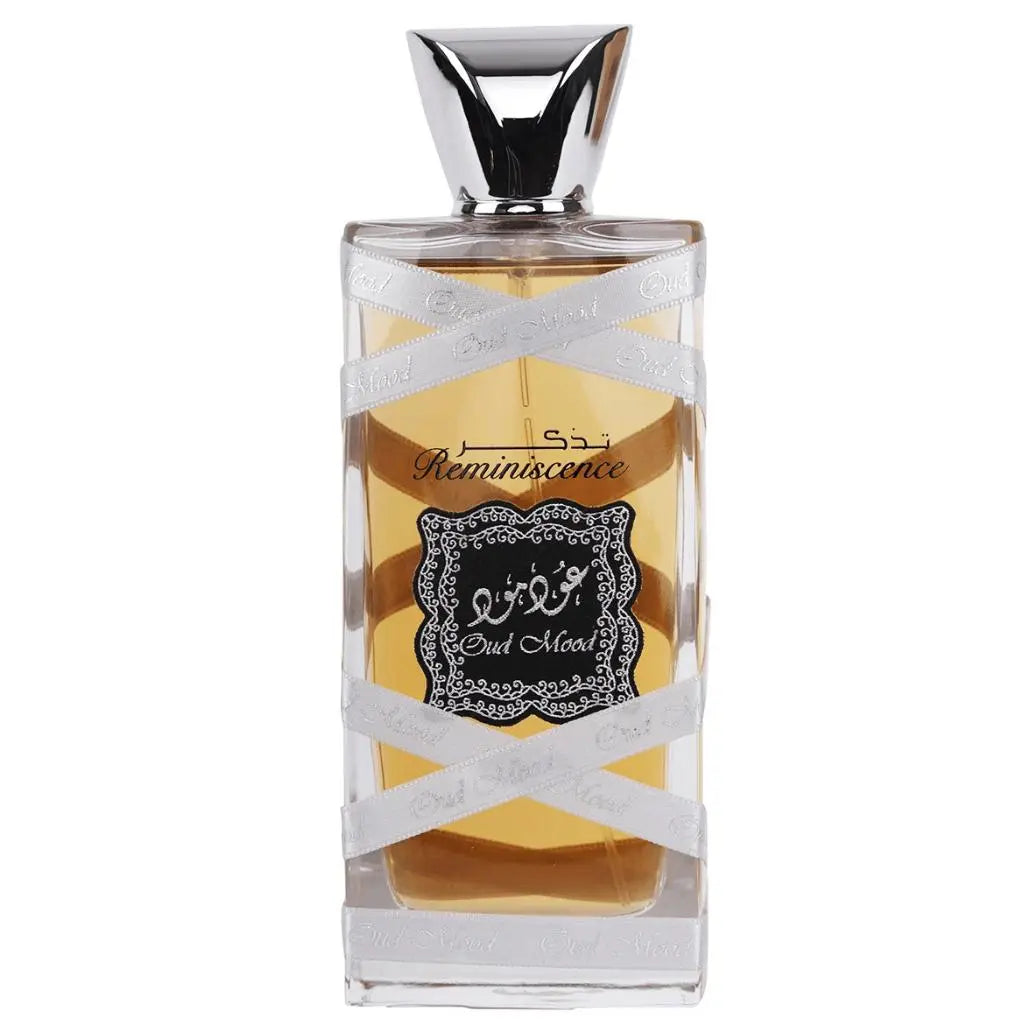 The image displays a perfume bottle with the following attributes:  The bottle is rectangular with a clear glass design, allowing a view of the amber-colored perfume inside. A silver ribbon with the words "Oud Mood" printed in a repeating pattern wraps around the bottle. The central label is ornate with a black background and white decorative border; it features Arabic calligraphy and the word "Reminiscence" in English script.