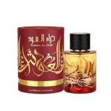 A perfume bottle with a gradient design transitioning from clear to red, with a black cap. It has gold Arabic calligraphy "THARA AL OUD" and the English subtitle "SUPREME INTENSE" on the lower part. Accompanying the bottle is a cylindrical maroon packaging with the same gold Arabic calligraphy and an English inscription. The packaging also states "SUPREME INTENSE" along the lower gold band.