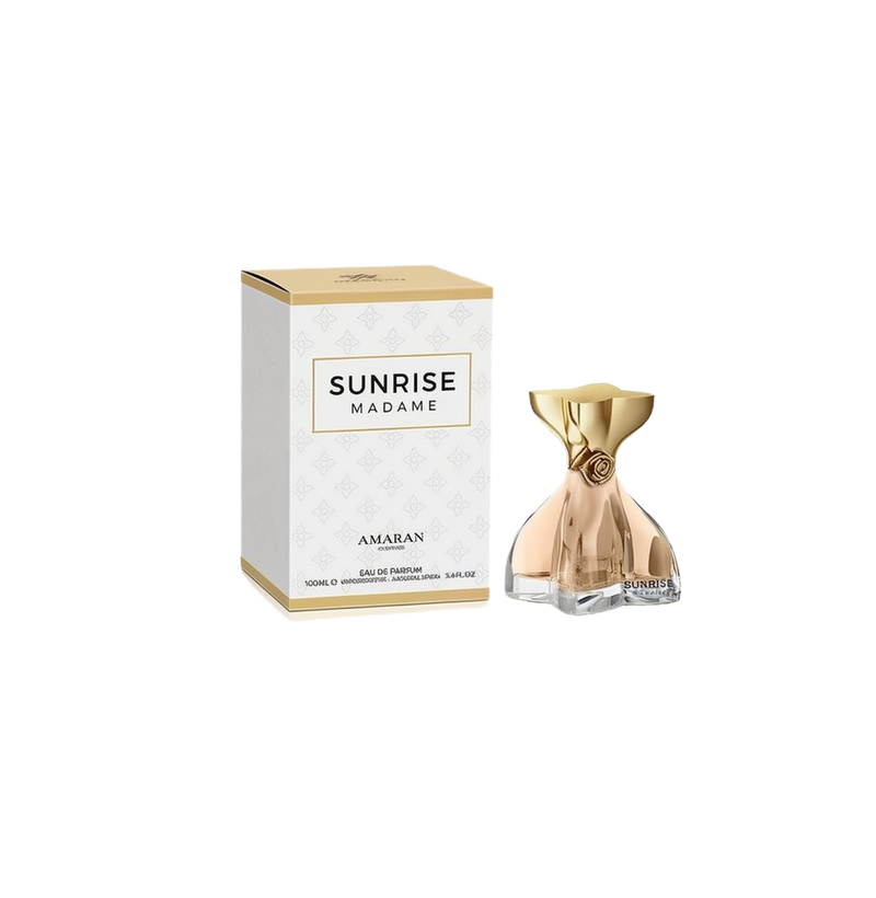 A feminine perfume bottle with a sculpted bow-like shape in a transparent peach hue, topped by a metallic gold cap featuring a small rose detail. The front reads “Sunrise Madame,” and the bottle is displayed next to a white and gold box marked “Sunrise Madame” by Amaran, indicating 100ml Eau De Parfum.