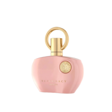 The image displays a perfume bottle from Afnan's "SUPREMACY" line. The bottle is made of smooth, matte pink glass and has a rounded, organic shape with a flat base, allowing it to stand upright. The cap is a glossy golden hue, designed with a loop that creates a visual focus and adds an element of luxury. On the front of the bottle is a golden emblem, adding a touch of elegance to the overall design. Below the emblem, in a simple and sophisticated font, reads "SUPREMACY AFNAN." 