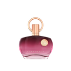 The image shows a perfume bottle with a distinctive design. It has a round, flat base with a gradient color that shifts from transparent to a deep pink hue towards the bottom. The cap is a metallic rose gold color, featuring a simple yet elegant circular design that loops around the nozzle. The front of the bottle has a metallic emblem with intricate detailing, adding a touch of luxury. The text on the bottle reads "SUPREMACY AENAN". 