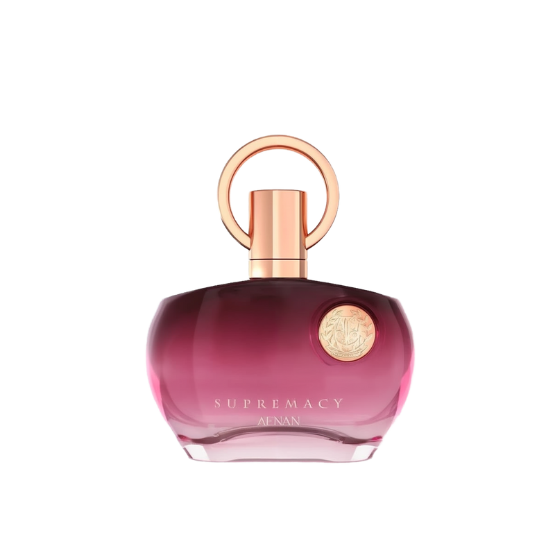 The image shows a perfume bottle with a distinctive design. It has a round, flat base with a gradient color that shifts from transparent to a deep pink hue towards the bottom. The cap is a metallic rose gold color, featuring a simple yet elegant circular design that loops around the nozzle. The front of the bottle has a metallic emblem with intricate detailing, adding a touch of luxury. The text on the bottle reads "SUPREMACY AENAN". 