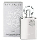 The image shows a product set from "AFNAN" featuring the "SUPREMACY" fragrance for men. On the left is the perfume's packaging box, which is a light grey with a subtle floral and vine embossed pattern, and the brand and product name printed in silver, reflective lettering. 