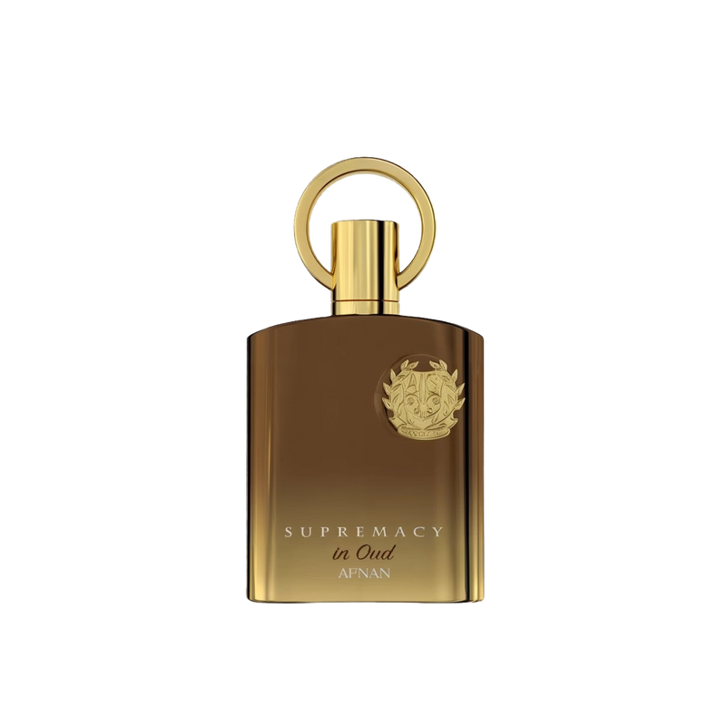 The image shows a luxurious perfume bottle with a sleek, modern design. The bottle appears to be made of a glossy, brown-gold glass with a golden cap that has a circular handle on top, giving it a unique and elegant look. The front of the bottle features a prominent emblem, likely a brand logo, embossed in gold which adds to the opulent aesthetic. Below the emblem, the words "SUPREMACY in Oud AFNAN" are printed in capital letters, indicating the fragrance name and brand. 