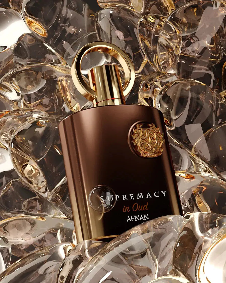 The image features a luxurious perfume bottle with a matte brown body and a polished golden cap, adorned with a round golden ring on top. The bottle is set against a mesmerizing background of reflective crystal-like shapes with gold accents, creating an opulent and dynamic backdrop. A detailed golden emblem is embossed on the front of the bottle, and below it, the perfume's name "SUPREMACY in Oud AFNAN" is written in elegant gold lettering.