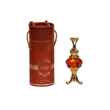The image features an ornate perfume oil set, consisting of a cylindrical red container with gold trim and decorative elements, and a luxurious golden and red glass perfume oil bottle with an intricate metallic design. The container has a lid with two golden, braided rope-like handles and displays the text "Supreme AMBER" in a decorative golden font, with a smaller inscription "Concentrated Perfume Oil 20ml" below. 
