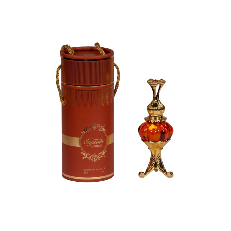 The image features an ornate perfume oil set, consisting of a cylindrical red container with gold trim and decorative elements, and a luxurious golden and red glass perfume oil bottle with an intricate metallic design. The container has a lid with two golden, braided rope-like handles and displays the text "Supreme AMBER" in a decorative golden font, with a smaller inscription "Concentrated Perfume Oil 20ml" below. 
