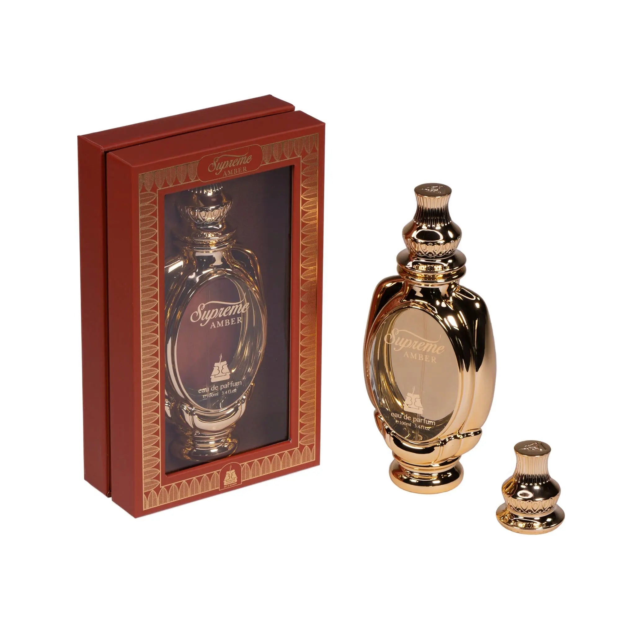 The image presents a luxurious perfume set, featuring a shiny golden-brown bottle with a traditional, rounded shape and an intricately designed cap. To the left, the matching packaging is a deep red box with a viewing window displaying the same bottle design and the words "Supreme AMBER" in elegant font, along with "eau de parfum" below. The box is adorned with golden patterns and trim that complement the bottle's design. 