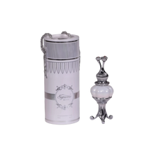 The image features two products on a white background. On the left, there is a cylindrical container with a silver chain, labeled "Supreme MUSK." Below the brand name is text that reads "Concentrated Perfume Oil 20ml." The container has a white label with elegant, decorative borders and a classic ornamental logo at the center. The top has an ornate design with a narrow middle that flares out at both ends, resembling a classic perfume applicator. 