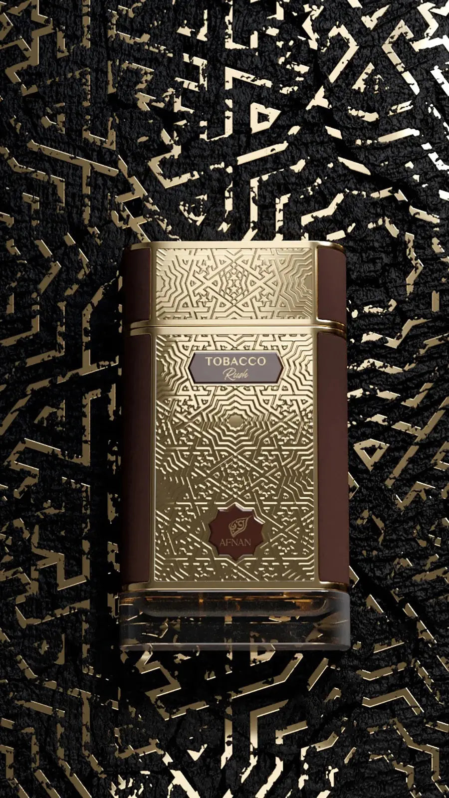 The image features a perfume bottle of "Tobacco Rush" by Afnan Perfumes. The background is an artistic, abstract design in black with gold accents, resembling fragmented calligraphy or a shattered gold leaf effect. The bottle is in the center with a square base, transitioning to a slightly narrower top. It has a rich, brown color with golden geometric patterns and the word "TOBACCO" prominently displayed in the center with "Rush" just below in a smaller font. 