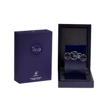 The image shows two items against a white background. On the left is a dark blue box with a matte finish and the brand name "Tribute by AFNAN" prominently displayed on the front. Below the name is additional text indicating that it is an "Eau de Parfum Vaporisateur" and the volume of "100ml, 3.4 FL. OZ." On the right side is an open box revealing a dark, navy blue interior with a textured surface. Inside the box is a vertical, ribbed navy blue panel.