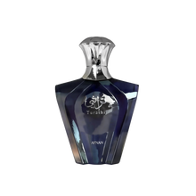 The image presents a sleek perfume bottle with a geometric design. The bottle has a deep blue color with a glossy, reflective surface, and features silver accents. The cap is silver and has an inverted cup shape that complements the bottle's shoulders. On the front, in silver lettering, is the name "Turathi" beneath an emblem with Arabic calligraphy, indicating the fragrance name or brand.