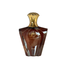 The image shows a perfume bottle with a unique geometric design. The bottle is a rich brown color with a reflective surface, giving it a glossy appearance. The cap is golden and shaped like an inverted cup, adding to the luxurious look of the bottle. On the front, there is Arabic calligraphy in gold, along with the word "Turathi" below it, suggesting the name or brand of the perfume. The word "AFNAN" is also visible at the bottom front of the bottle, indicating the manufacturer or designer of the perfume. 