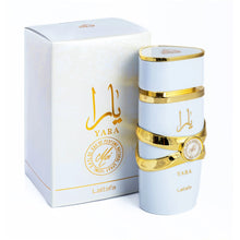 The image shows a cylindrical perfume bottle for "YARA Moi" by Lattafa, accompanied by its packaging. The bottle is matte white with gold bands and features the brand name "Lattafa" at the bottom. It has a ribbon-like gold band around its center with a ro