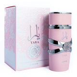 This image features the perfume "YARA" by Lattafa, displayed next to its packaging. The cylindrical bottle is pale pink with silver bands, mirroring the previous description. The packaging is a square box with a matching pale pink color and a subtle floral pattern embossed on it, adding a delicate texture. The perfume name "YARA" is prominently displayed in a darker pink shade with the Arabic script above and the phrase "EAU DE PERFUME NATURAL" in a circular silver emblem. 