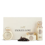 The image shows two perfume bottles from Gissah's "Endless Love" collection, displayed in front of a cream-colored box that has the collection's name printed on it. One bottle is short and wide with a flat cap, while the other is tall and cylindrical with a rounded cap. Both bottles are an off-white color and feature ornate gold medallions. Next to the bottles are a cluster of dark-colored items that resemble cloves, which might indicate the scent profile of the perfumes.