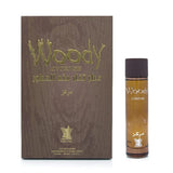 The image shows an elegant perfume product which includes a bottle and its box. On the left, there's a dark wood-textured box with the words "Woody Intense" in raised, green lettering. Below, there is Arabic script and a gold emblem of a crown. The right side of the image presents the perfume bottle, which has a gradient design going from clear to brown at the base, with the same "Woody Intense" branding as on the box. Below the name is an Arabic translation, and the bottle cap is a dark, opaque brown. 