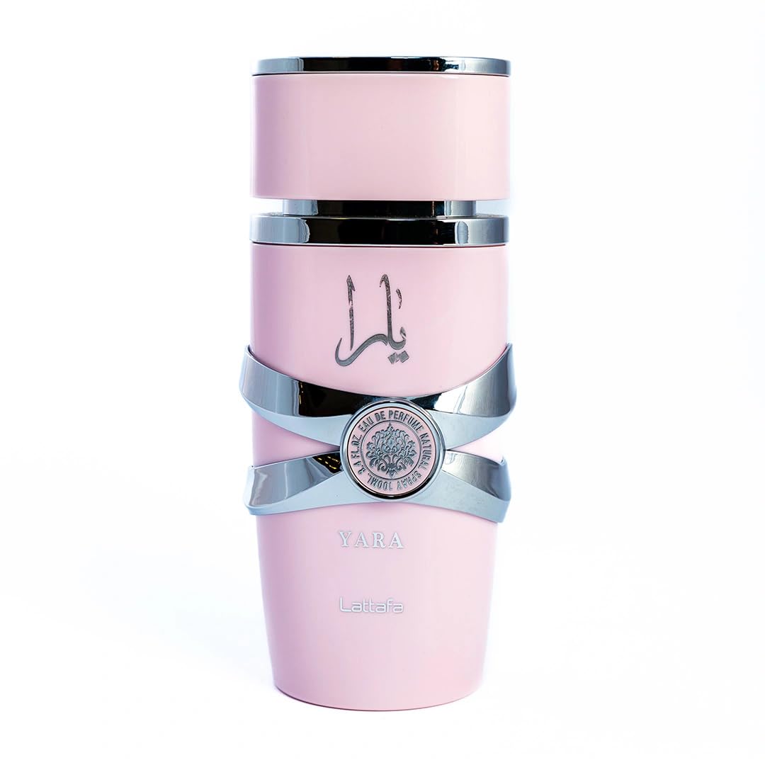 This image depicts a cylindrical, pale pink perfume bottle with the name "YARA" from the brand Lattafa. The bottle has a unique stacked design with silver bands wrapping around it, giving the appearance of three separate sections. The upper and lower sections are matte pink, while the middle section is glossy black, providing a striking contrast. A silver emblem with intricate detailing is centered on the middle band. The Arabic script, likely the name "YARA," is printed in black on the upper pink section.