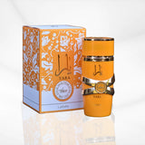 The image showcases an orange cylindrical perfume bottle labeled "YARA" by Lattafa next to its packaging. The bottle features a glossy finish with two silver bands and a central gold ribbon-like band that holds a round gold emblem.  The box also has the name "YARA" and what appears to be a silver emblem similar to that on the bottle. Both the bottle and the packaging are placed on a reflective surface.